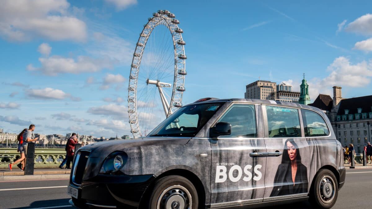 A fully electric London taxi in a full wrap livery beside the London Eye