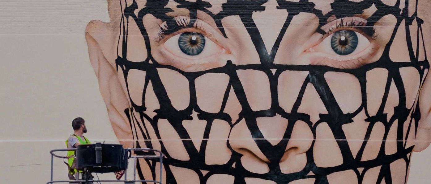 A signwriter on a raised platform dwarfed by an enormous hand-painted face on the side of a building