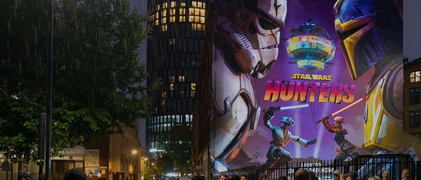 A brightly lit hand-painted advertisement on a building at night with people gathered in front of it