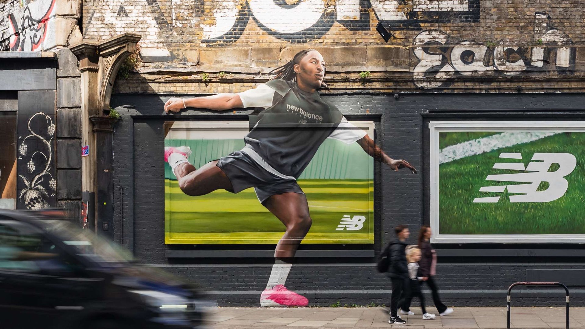 A hand-painted advertisement of a footballer covering a brick building beside a road, with traffic passing and people walking by