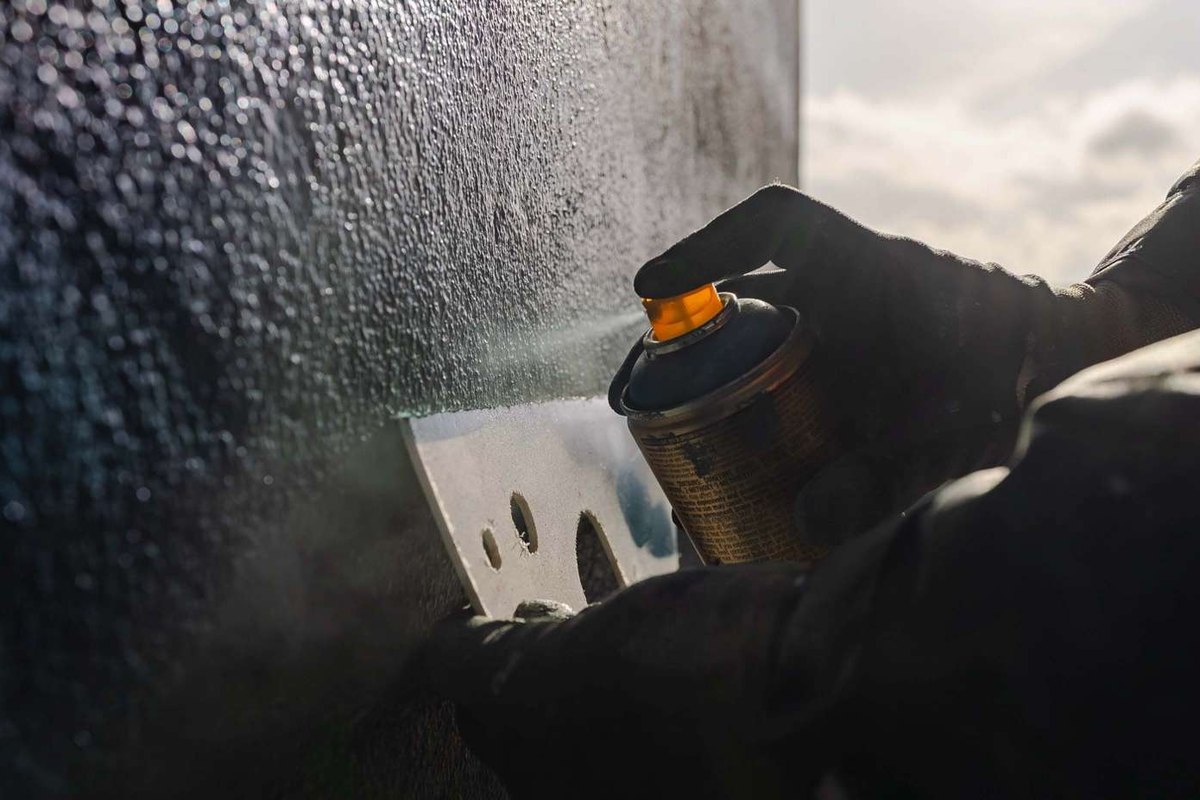 A close view of a gloved hand spraying paint through a stencil onto a textured wall