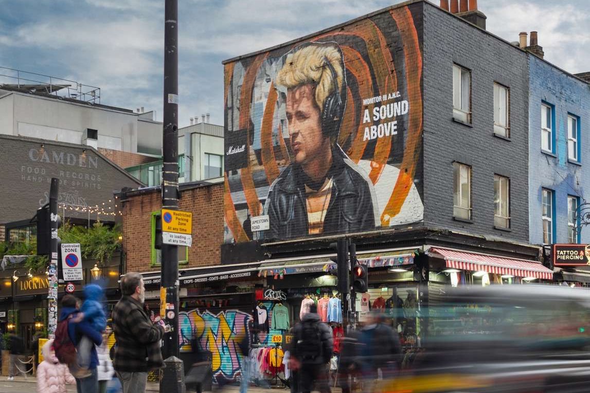 A hand-painted portrait on a building above a busy shopping street with traffic and pedestrians