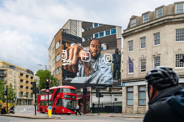 A building end painted with a portrait of a man reaching towards the viewer