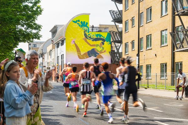 Runners passing a wall painted with a figure in bright flat colour