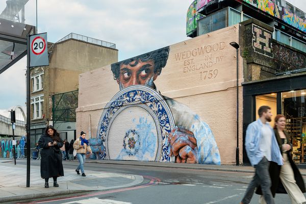 A brick wall painted with a blue and white patterned plate held by two hands