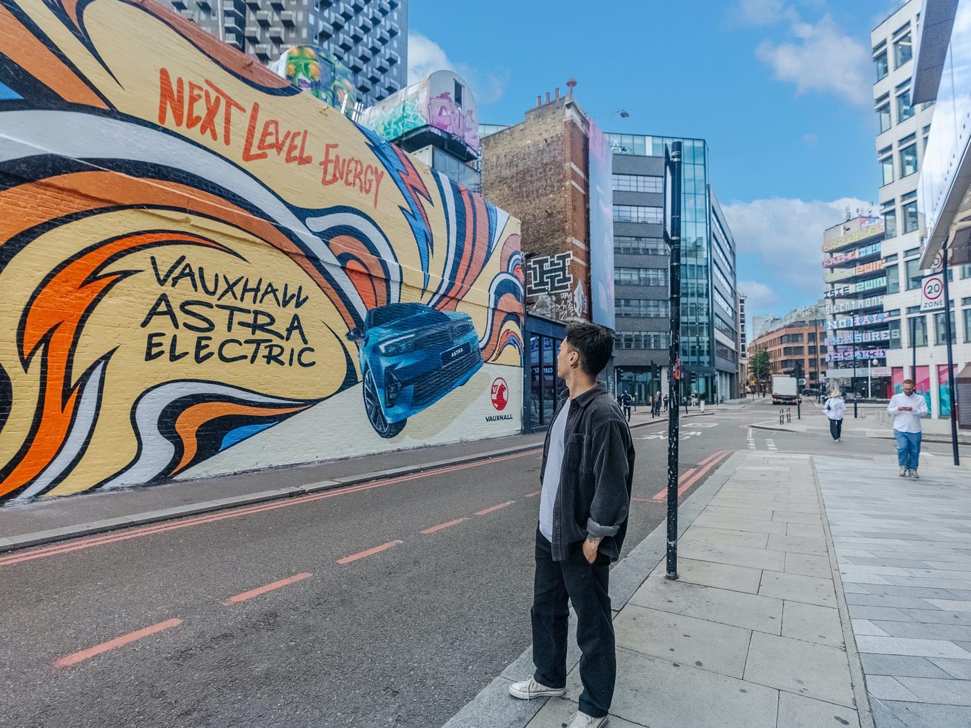 A person pausing on the street to look up at a large painted wall