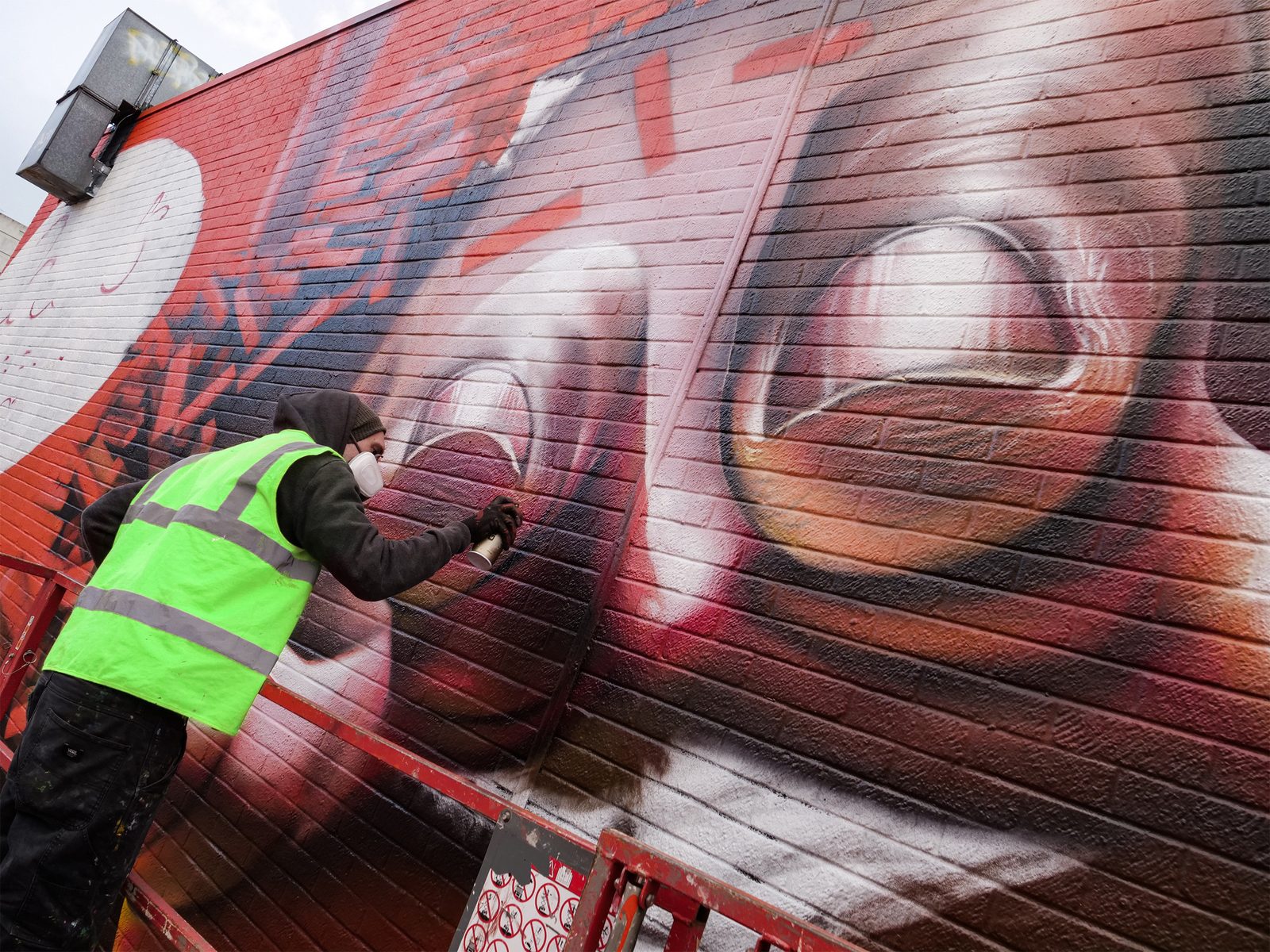 An artist on a lift, dwarfed by the face he is hand-painting