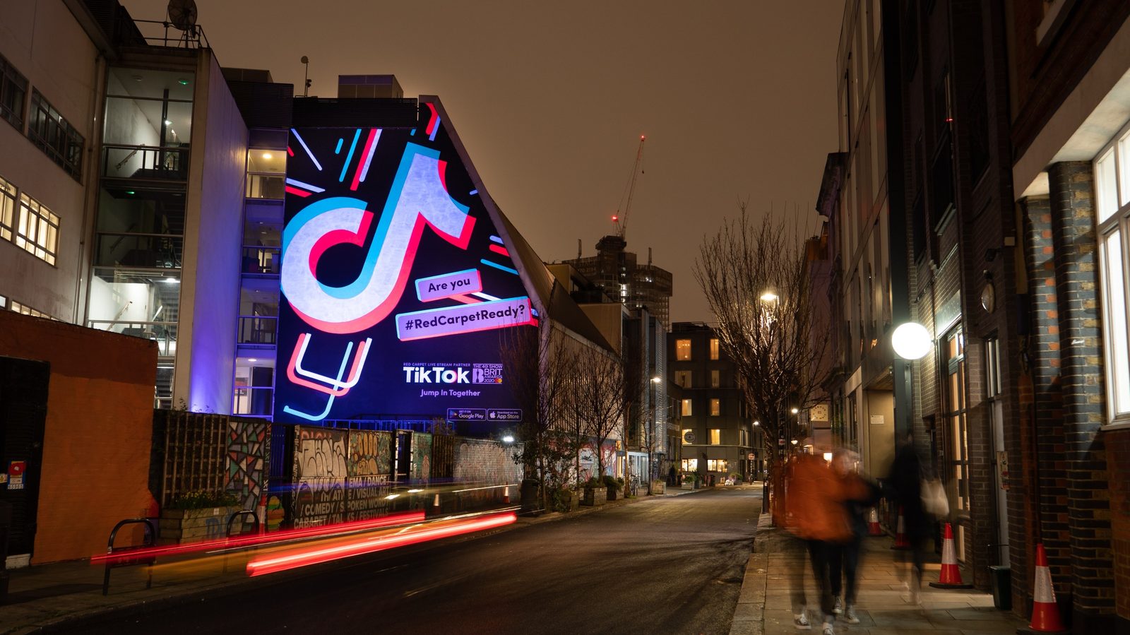 An illuminated hand-painted mural lighting a London street after dark