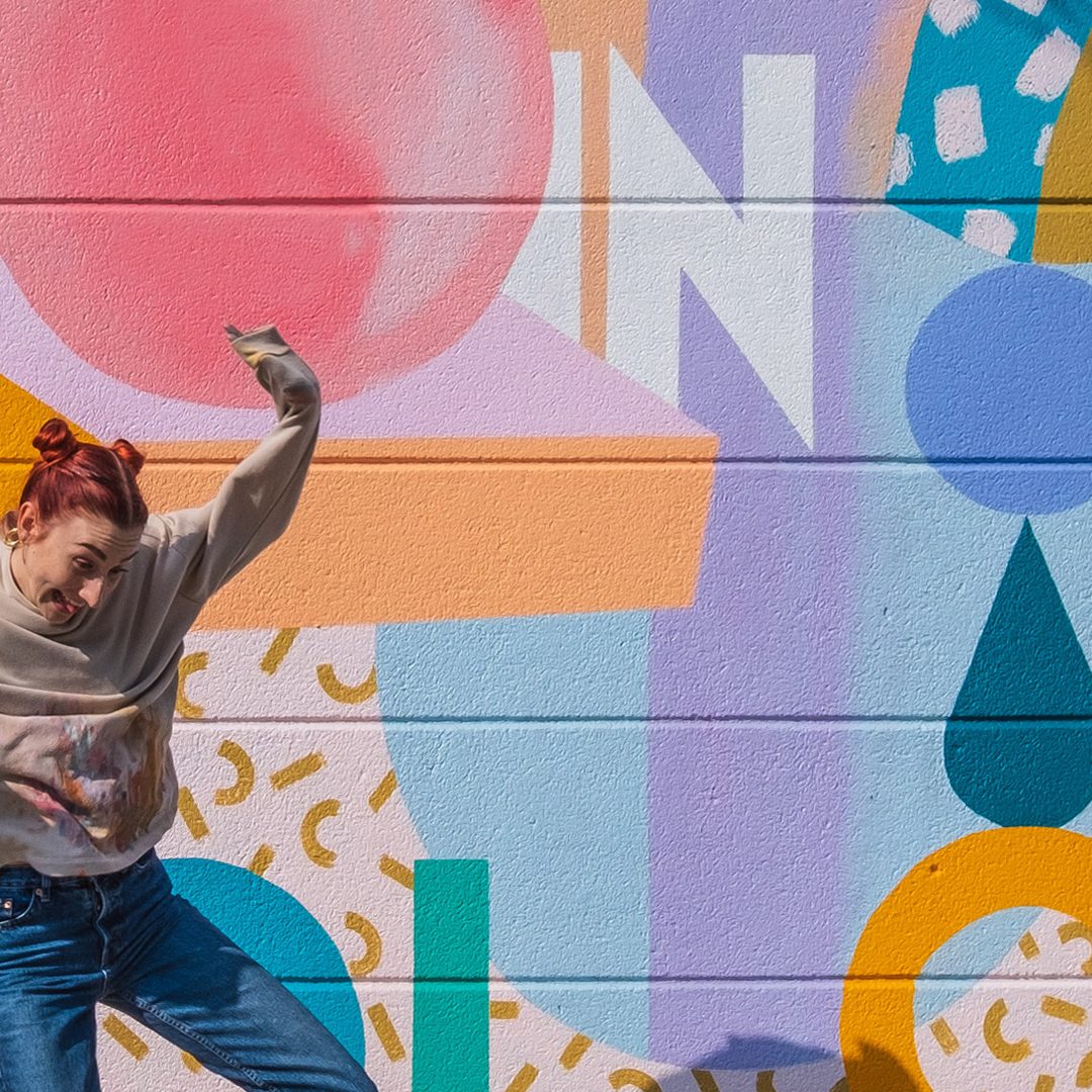 A woman posing in front of a bright, boldly patterned hand-painted wall