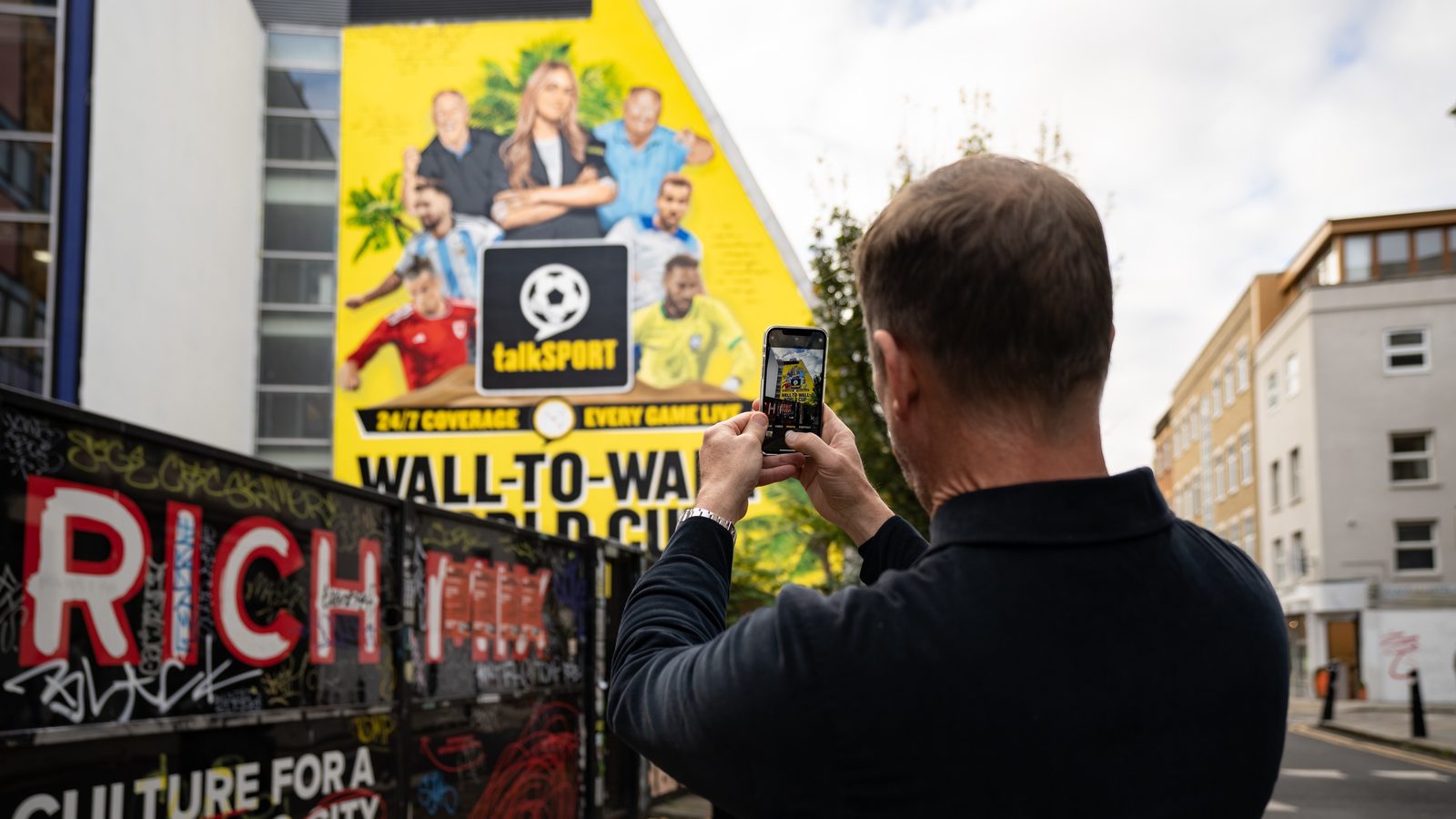 A man stopping on the pavement to photograph a hand-painted wall