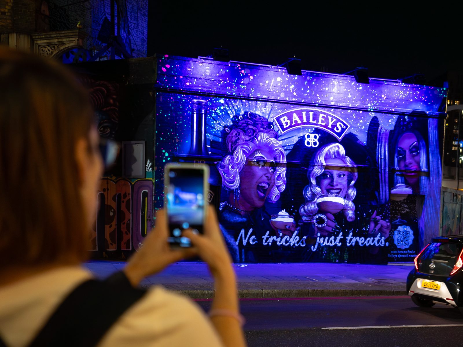 A woman stopping to photograph an illuminated brand mural at night