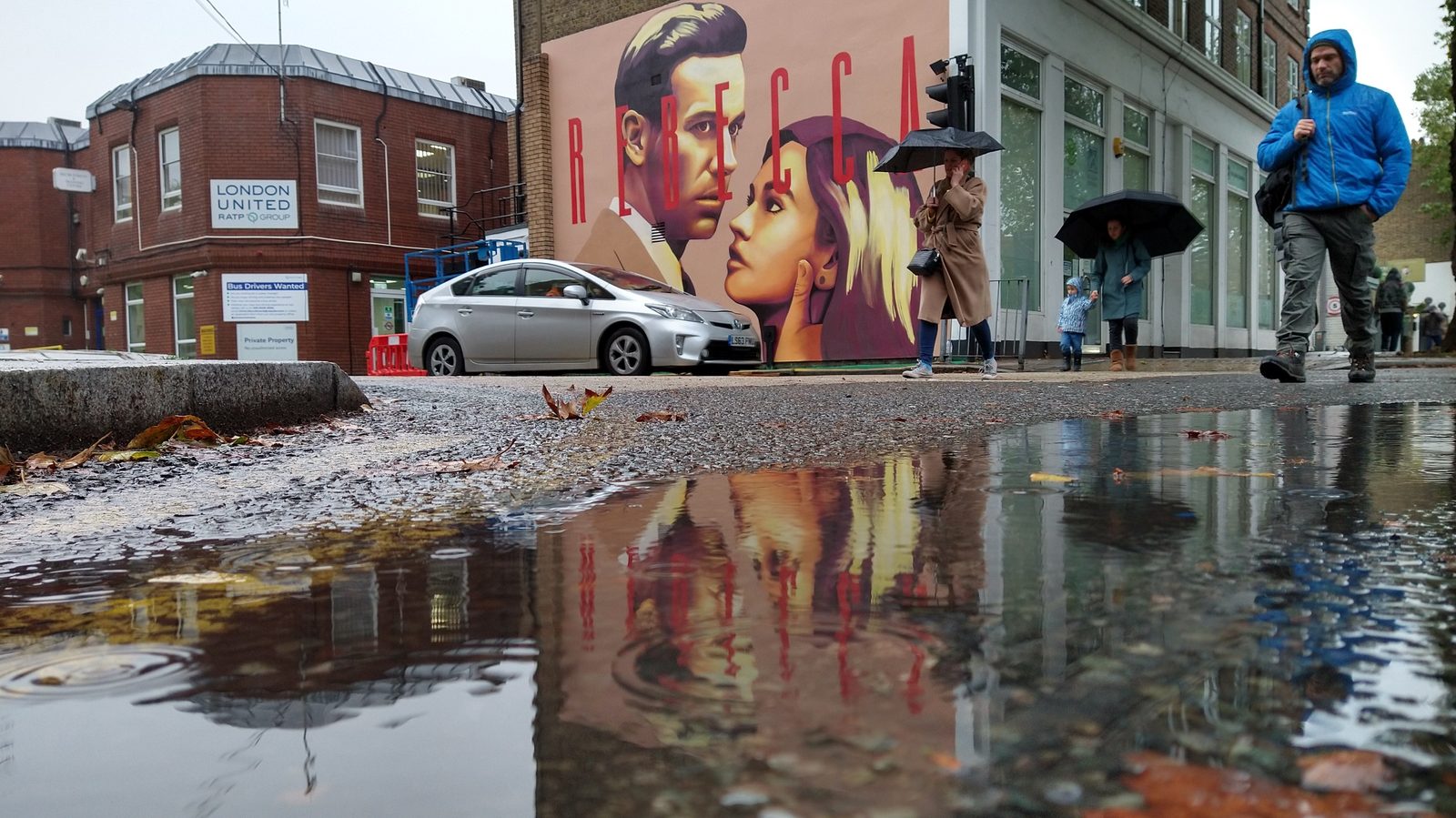 A hand-painted wall reflected in a puddle on its own rainy street