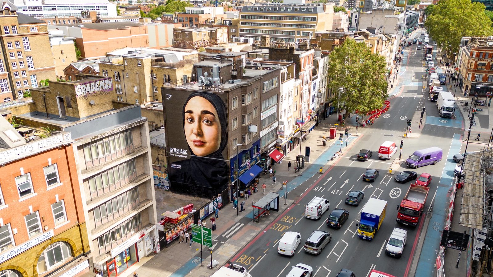 A tall portrait mural on a building above a busy London street