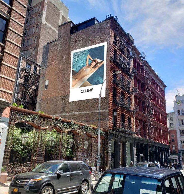 A tall painted wall rising above a cobblestone SoHo street lined with shops and restaurants